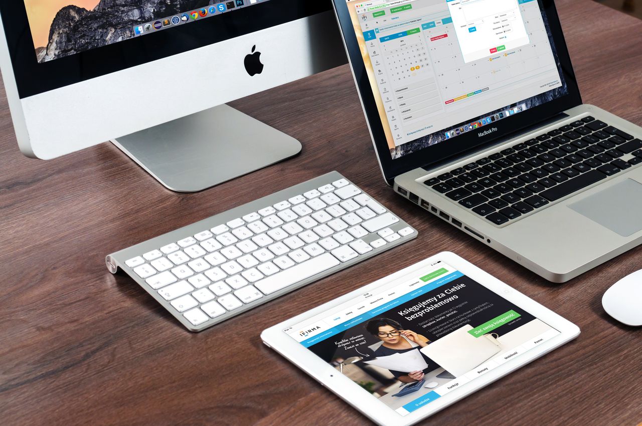 A polished office desk arrangement featuring Apple devices: iMac, MacBook, and iPad.